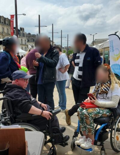 Journée de la Solidarité 2025 : groupe de participants, dont deux personnes en fauteuil roulant, devant le stand